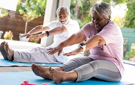 Un couple plus âgé assis sur son tapis de yoga, essayant de toucher leurs pieds