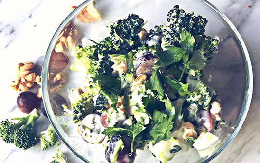 Un bol transparent rempli d'une salade de broccoli, noix et raisin