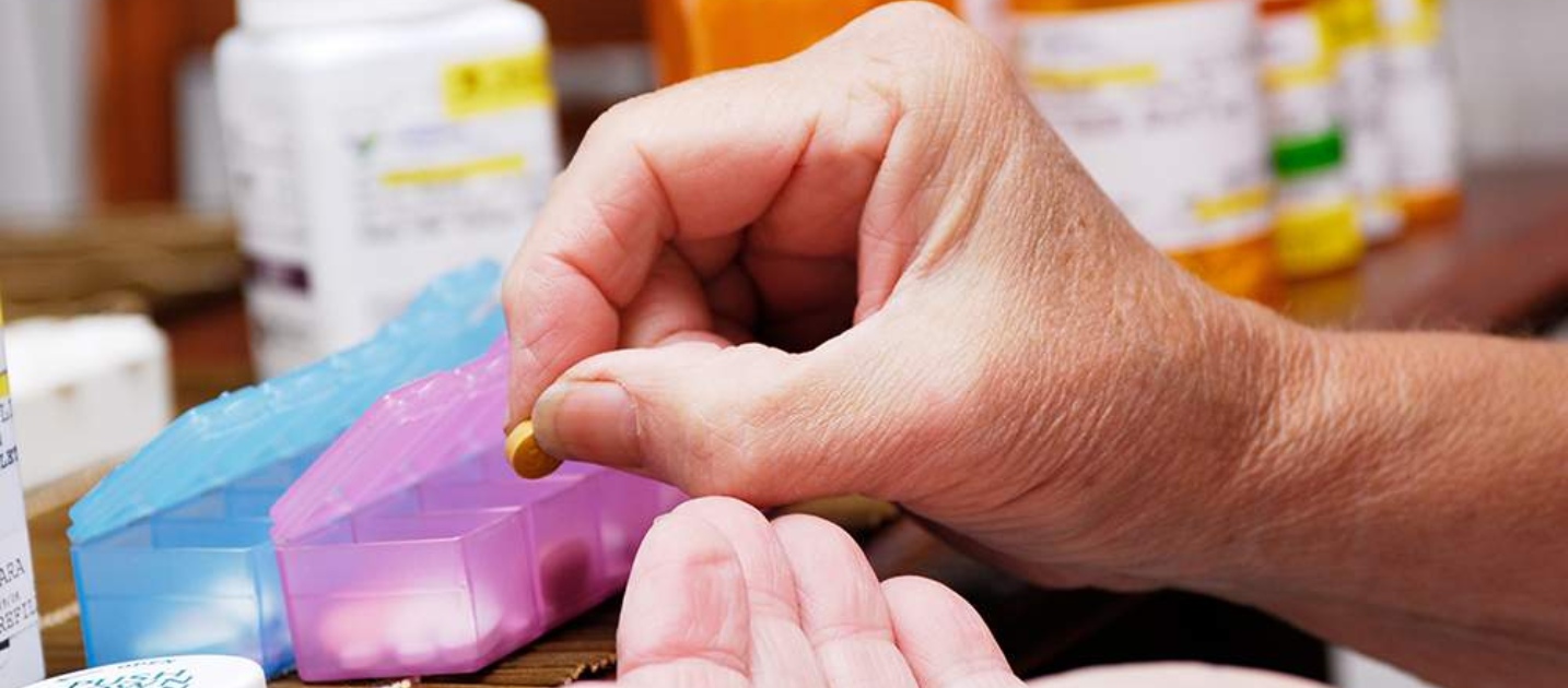 Une main prenant un comprimé dans une boite à médicaments de couleur rose