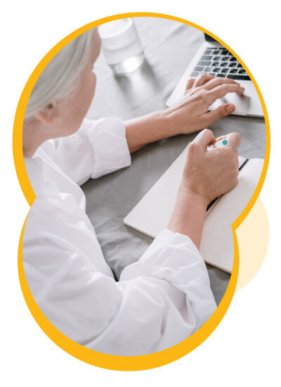 Une femme agée écrivant sur un cahier et utilisant un ordinateur portable