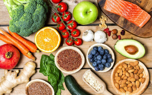 A variety of healthy foods are shown, including salmon, broccoli, avocado, beans, tomatoes, and whole grains