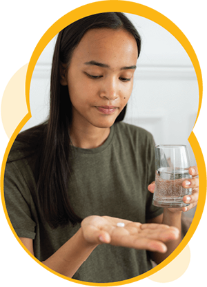 Une personne à la peau moyennement foncée tenant un verre d’eau dans une main et une pilule dans l’autre.