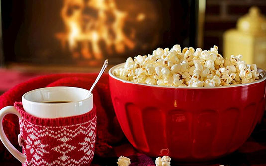 Une tasse et un bol de popcorn devant un feu de cheminée