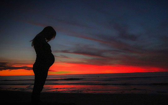 femme enceinte sur la plage au couché de soleil