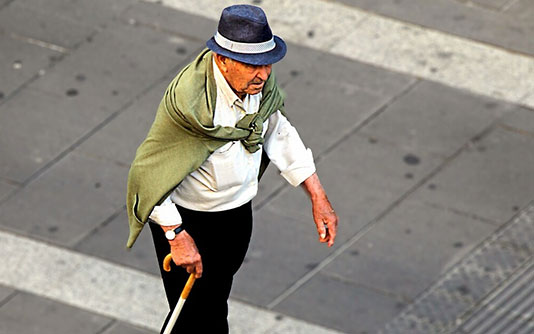 Un homme agé traversant une rue à l'aide d'une canne
